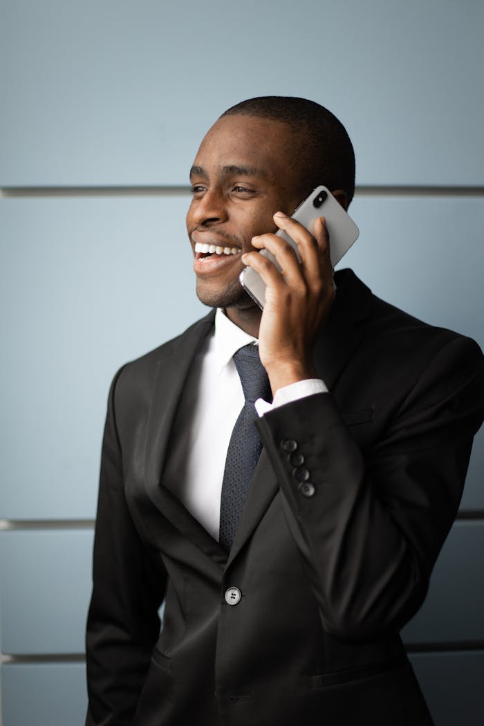 Confident African American businessman smiling while talking on phone in formal attire.