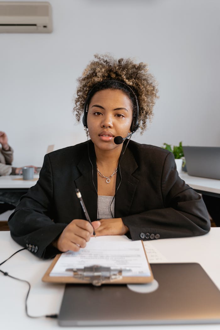 Woman in professional office setting using a headset and clipboard, focused on customer service.